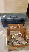 Blue Mastercraft toolbox with handle, two cardboard boxes in front containing assorted hardware and fasteners