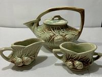 Front view showing teapot, creamer, and sugar bowl with detailed pine cone design