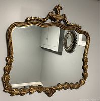 Full front view of the antique gilded ornate mirror showing the carved floral frame and decorative crest with urn.