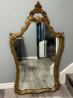 Full view of large antique gilded mirror showing entire frame and reflective surface.