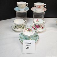 Photo showing five tea cups with matching saucers elevated on clear stands and arranged on white surface against black background.