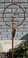 Front view of the copper lawn sprinkler showing the circular top with a spiral coil mounted on a copper stake placed in the garden soil.