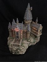 Porcelain Hogwarts Castle with lit fiber optic lights glowing orange, showing fine stone and snow detailing, with visible chip damage.