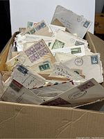 Image of a cardboard box filled with a variety of vintage postal envelopes and first day covers showing different stamps and markings.