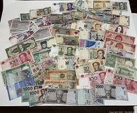 Photo shows a collection of various international banknotes spread out on a flat surface, including notes from Indonesia, Argentina, Venezuela, China and more.