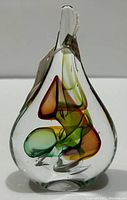 Front view of clear tear drop-shaped crystal paperweight with colorful internal shapes in green, amber, and brown hues, showing the attached label.