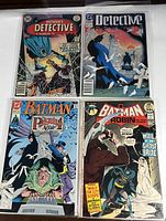 Four Batman comic books in protective sleeves, arranged in a 2x2 grid, showing covers from Detective Comics and Batman series.