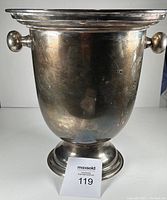 Front view of vintage silver plated champagne bucket with round knob handles and pedestal base showing surface wear.
