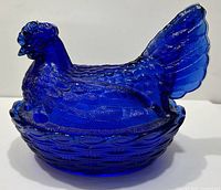 Side view of cobalt blue slag glass hen on nest candy dish showing detailed feather and tail split.
