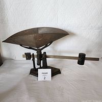 Side angled view of vintage grocery scale showing cast iron base, metal tray, balancing arm, and counterweight