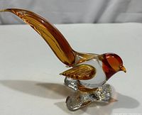 Side view of Murano glass bird showing amber head, clear body, amber wings, and long amber tail on clear branch base