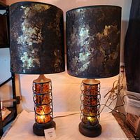 Pair of vintage dual light table lamps with multicolored lucite cylindrical bases encased in metal ring design and mottled brown shades, both lit and shown from front.