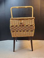 Wicker sewing basket with handle and four wooden legs attached, side view showing texture and latch.
