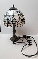 Full view of vintage stained glass lamp showing the stained glass shade and brass base with electrical cord.