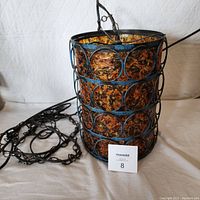 Front and side view of the vintage swag light showing the blue metal frame and amber lucite inserts along with hanging chain and black cord on white backdrop.