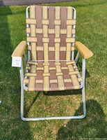 Front view of the vintage lawn chair showing the intact woven webbing and wooden armrests on an aluminum frame.