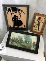 Three framed artworks including a silhouette reverse painting, feather bird art, and fox hunt print on white table