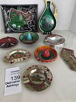 Image showing all nine vintage ashtrays arranged on a white surface with varying shapes, colors, and designs, including one shaped like Texas with map and landmarks.
