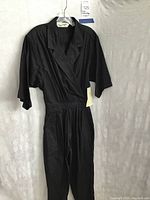 Front full-length view of black Diane Von Furstenberg jumpsuit on hanger against white background.