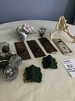 Photo showing assorted door hardware including porcelain knobs with floral patterns, glass knobs, metal door plates and two green metal hinges.