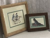 Pair of Native American prints framed; left larger Greig horse print with light wooden frame, right smaller Pena figure print with dark wooden frame. Both prints show matting and frames have scuffs.