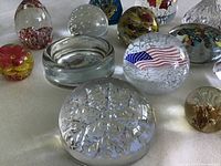 Top surface view displaying multiple glass paperweights arranged, showcasing floral, bubble inclusions, American flag, and abstract swirls.