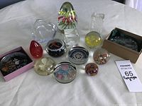 Front view of all fourteen paperweights arranged together on a white cloth, showing various shapes and designs.