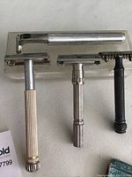 Photo showing four vintage razors on a plastic storage case including a open comb Gillette and other models.