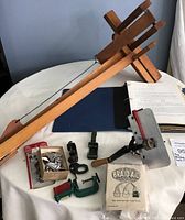 Photo showing wooden braiding frame, various clamps, metal tips, hand roller, and instruction binder on table.