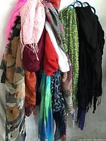 Photo of multiple scarves in various colors and fabrics hung on blue hangers showing patterns and textures.