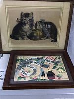 Full view of framed Meta Pluckebaum Sweet Tooth print with two kittens and framed Margo Alexander print with colorful script and folk art scene side by side on a surface