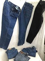 Wide shot showing six pairs of jeans laid out, including two blue denim Chic jeans, one black denim, and three Lee jeans folded.