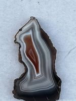 Front view of the natural agate cabochon pendant showing earthy white, gray, and reddish-brown bands with polished face and rough natural edges.