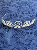 Front view of vintage Weiss tiara showing spiral rhinestone design on silver-tone metal frame against blue fabric background.