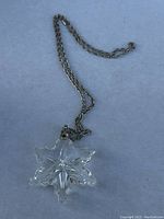 Clear crystal snowflake pendant necklace laid flat on a light surface, showing detail of the facets in the pendant and attached silver-tone chain.