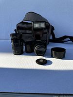 Minolta camera lot showing camera body with attached lens, telephoto zoom lens, flash unit, lens hood, body cap, and carrying case.