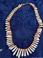 Full view of Victorian Deco necklace with white mother of pearl pickets and red coral beads on a dark blue fabric background.