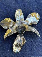 Close-up photo of a silver tone orchid flower brooch with gold tone accents showing detailed petals and naturalistic textures.
