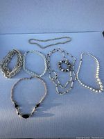 Eight shell jewelry pieces laid flat on a surface, including necklaces and one bracelet, showcasing various shell types and bead designs.