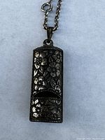 Front view of silver tone whistle pendant with floral engraving on a chain necklace.