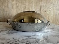Oval stainless steel roasting pan with high polished finish and matching domed lid with stainless steel handle and side loops.