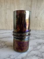 Front view of iridescent purple gold glass tumbler showing connected cylindrical shapes and smooth reflective surface.