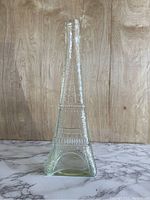 Front view of vintage clear glass Eiffel Tower shaped bottle on marble surface with wood background.