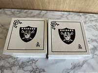 Two closed white boxes with Raiders logos and small holly decorations on the lid.