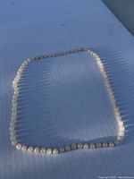Full view of the vintage white jade bead necklace laid out on a blue surface in natural light.