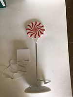 Full view of the 13 inch lighted peppermint candy decoration on a metal pole with a round base, accompanied by a power cord and plug