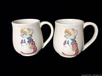 Photo of two ceramic coffee mugs featuring Susan Wheeler's Holly Pond Hill mouse designs, showing front side with 3D mouse carrying basket.