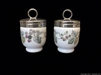 Front view of two porcelain egg coddlers with detailed blackberry designs and silver-plated lids with ring handles, showing design and condition.