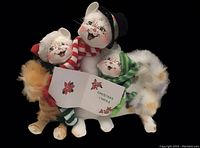 Front view of three Christmas caroling cats holding a carol book with floral designs, including an orange tabby, calico, and white cat.