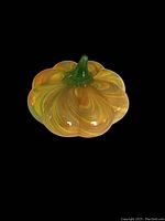 Top-down photo of a small art glass pumpkin with yellow and green swirl pattern, showing detailed ridges and a green stem.